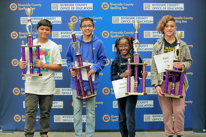 Four students stand holding large trophies