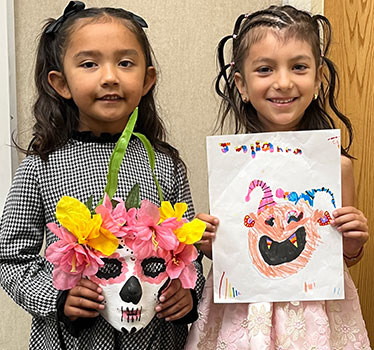 Two kindergarten girls holding their Dia de los Muertos artwork