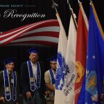 Operation Recognition graduates stand by flags of the armed services wearing graduation caps and stoles