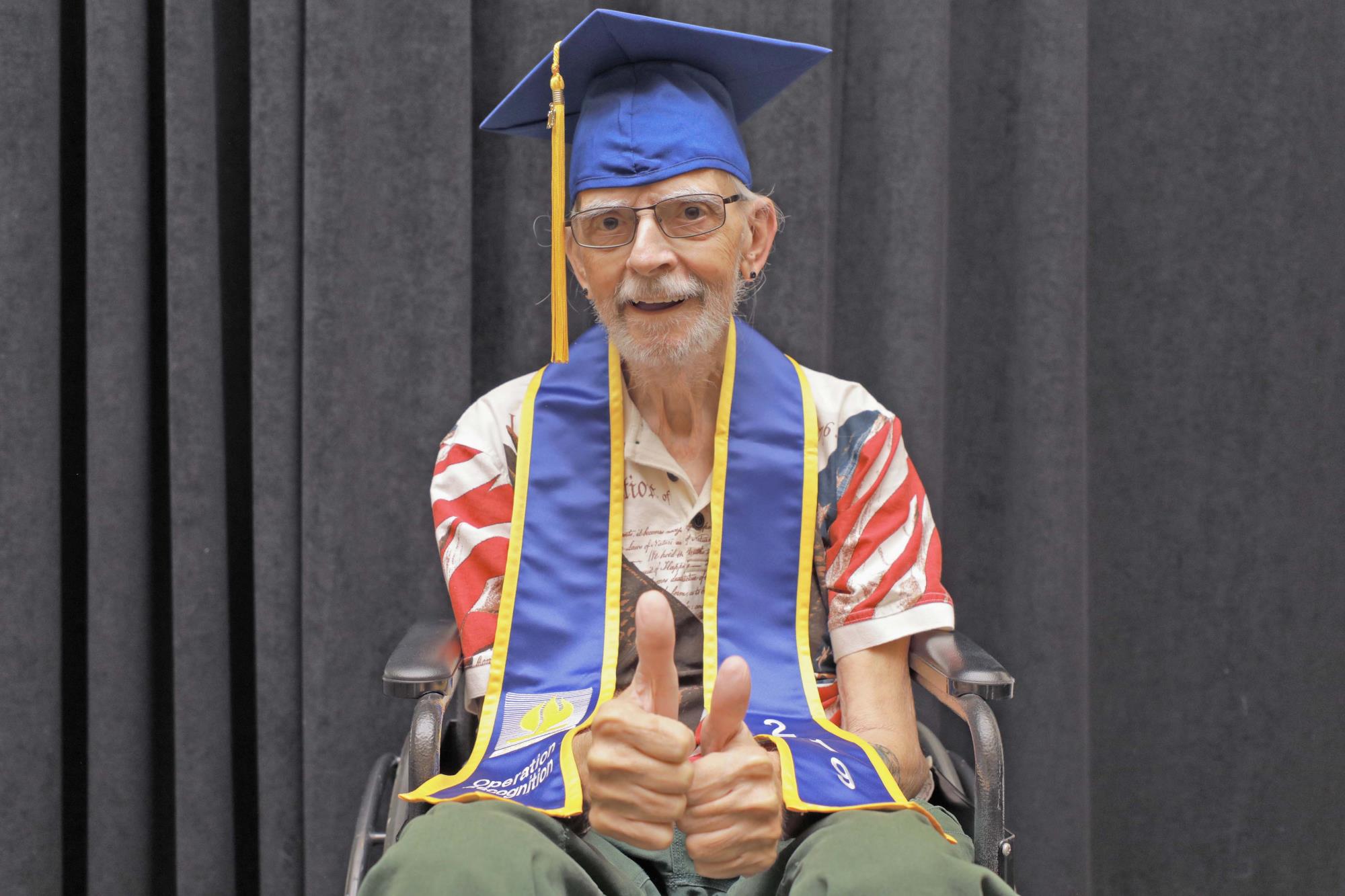 Veteran Franklin Stevens in graduation gear gives a double thumbs up