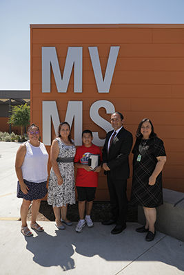 Diego holds his iPad on MVMS campus with Dr. Gomez, Dr. Root, and two other educators