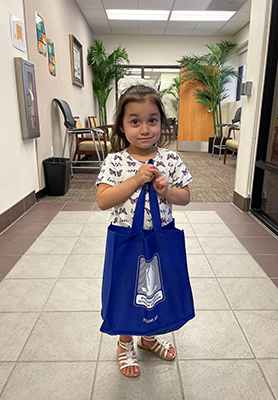 Keyla stands in a school office hallway holding an RCOE bag
