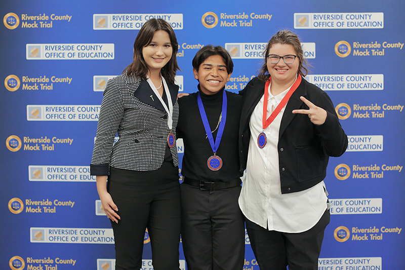 Three student honorees pose in front of Riverside County Mock Trial backdrop