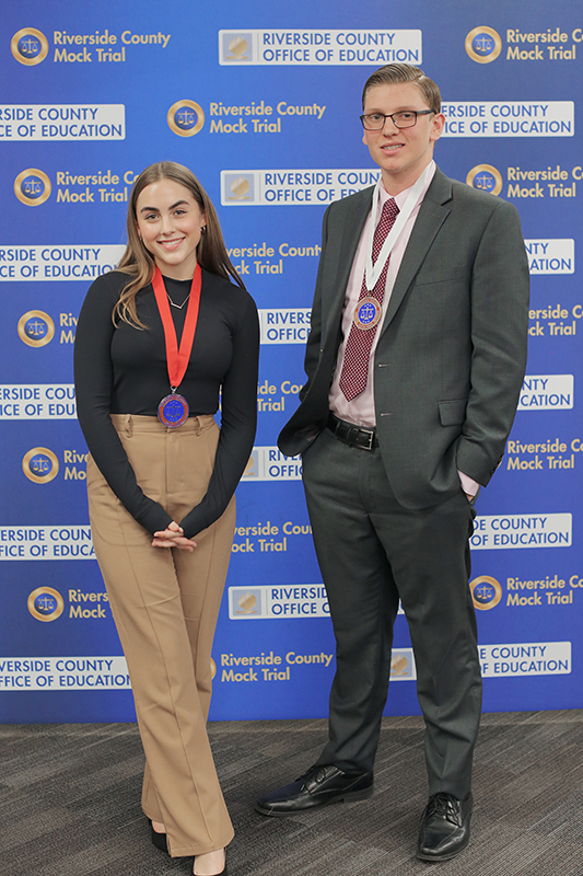 Two student honorees pose in front of Riverside County Mock Trial backdrop