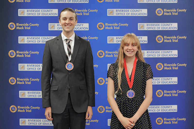Two student honorees pose in front of Riverside County Mock Trial backdrop