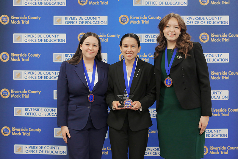 Three student honorees pose in front of Riverside County Mock Trial backdrop